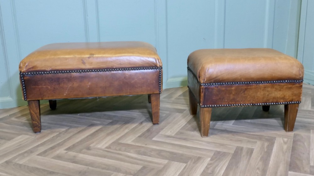 A pair of rectangular tan leather library footstools with close-studded trim detailing on tapered square wood legs. View II