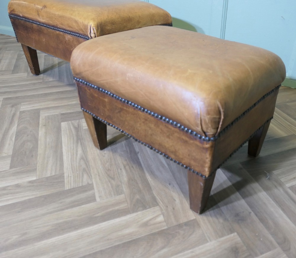 A pair of rectangular tan leather library footstools with close-studded trim detailing on tapered square wood legs. View V