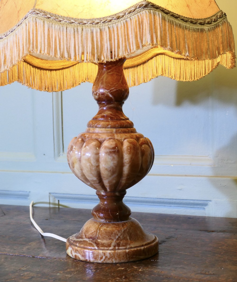An Art Deco table lamp featuring a carved variegated brown marble urn base and a flared beige lampshade with fringe details. View IV