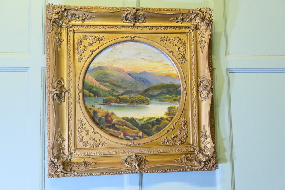 A Victorian oil landscape painting depicting mountains and a lake, set inside a circular aperture framed by a heavy square gilded gesso frame. View III