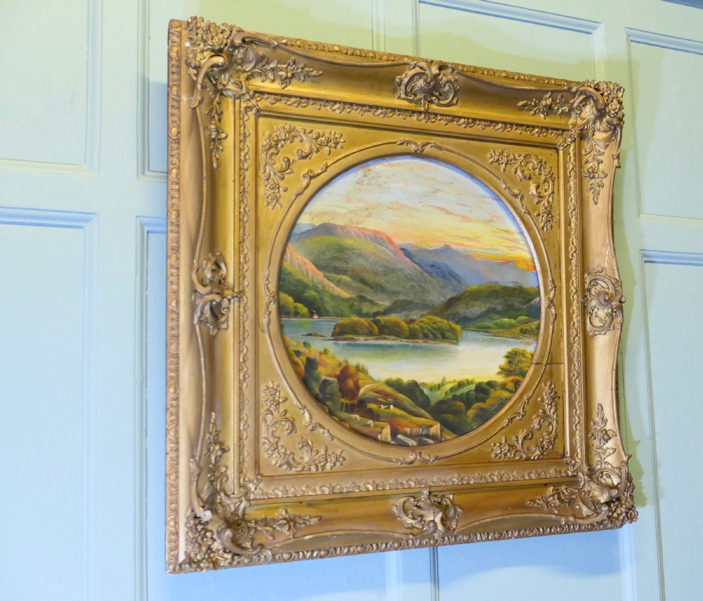 A Victorian oil landscape painting depicting mountains and a lake, set inside a circular aperture framed by a heavy square gilded gesso frame. View V