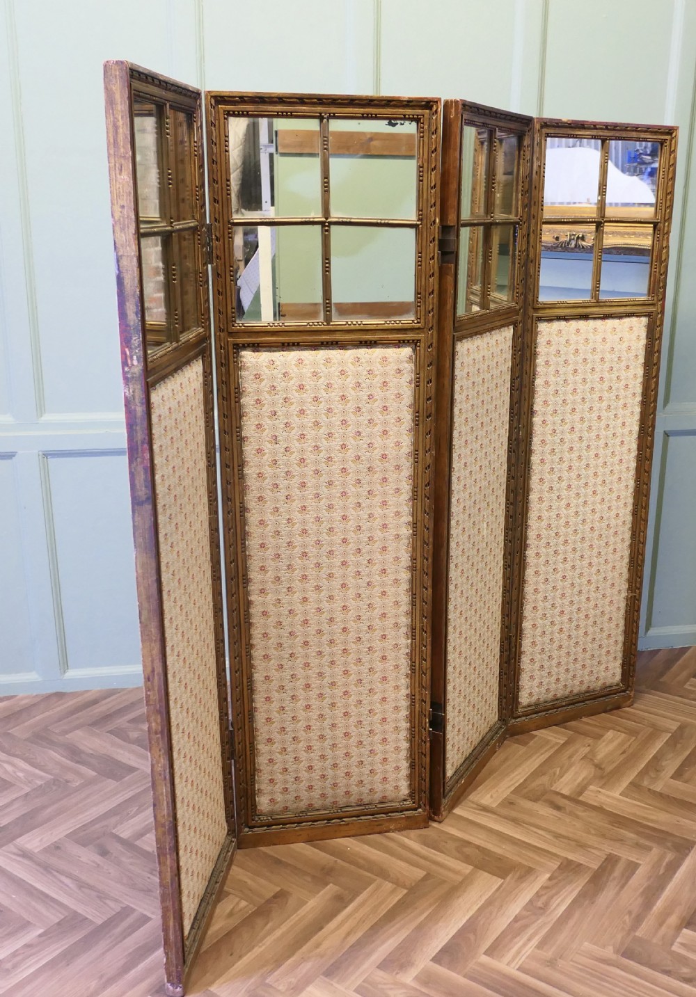 A four-panel French folding screen featuring gilded wood frames, glazed mirror panes at the top, and upholstered fabric lower sections.