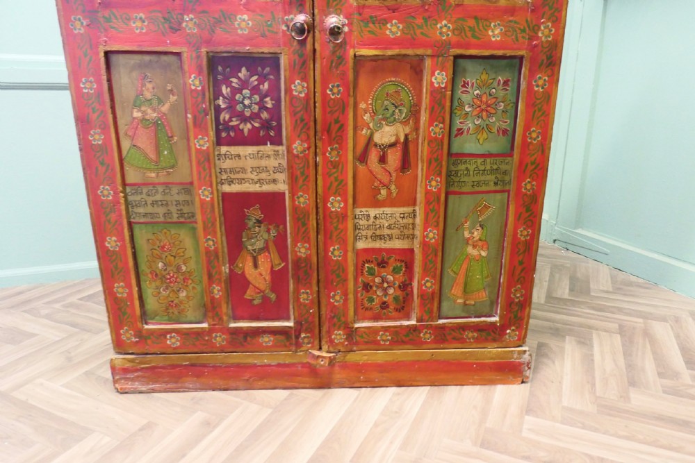 A tall red hand-painted Indian wooden cupboard decorated with framed panels featuring deities, figure artwork, Devanagari script, and floral motifs. View II