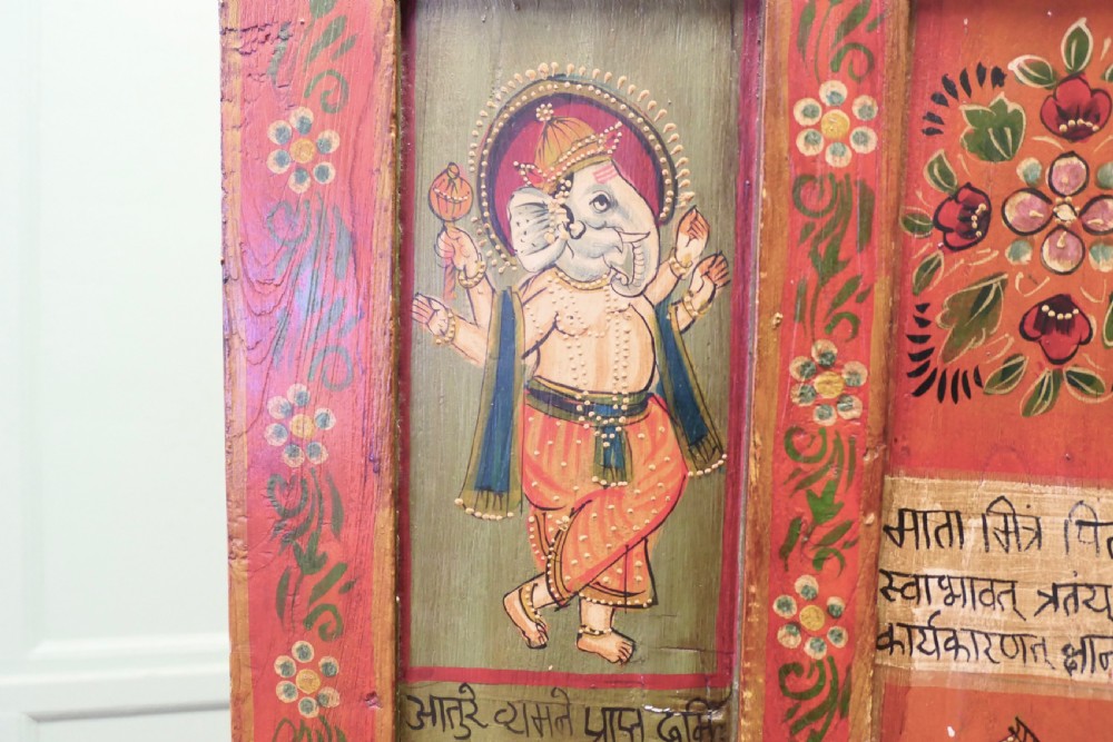 A tall red hand-painted Indian wooden cupboard decorated with framed panels featuring deities, figure artwork, Devanagari script, and floral motifs. View III