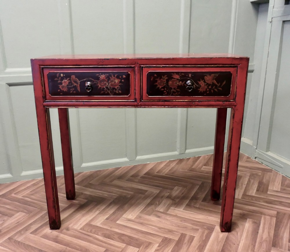 A red lacquered rectangular console table featuring two dark drawers decorated with painted floral motifs and metal ring handles on square legs.