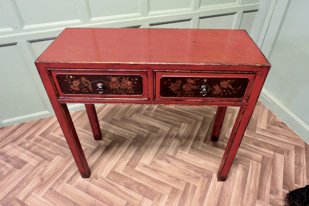 A red lacquered rectangular console table featuring two dark drawers decorated with painted floral motifs and metal ring handles on square legs. View II