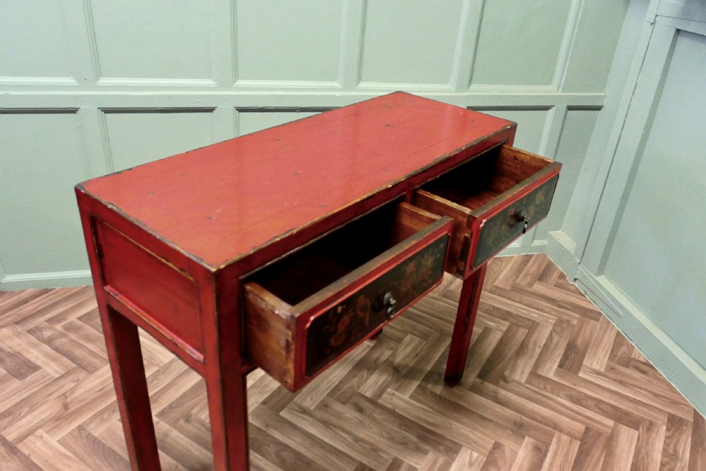 A red lacquered rectangular console table featuring two dark drawers decorated with painted floral motifs and metal ring handles on square legs. View VI
