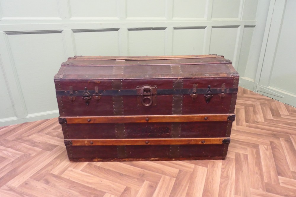 An antique dome top steamer trunk featuring dark canvas casing, polished oak slats, metal banding, and side leather handles. View III