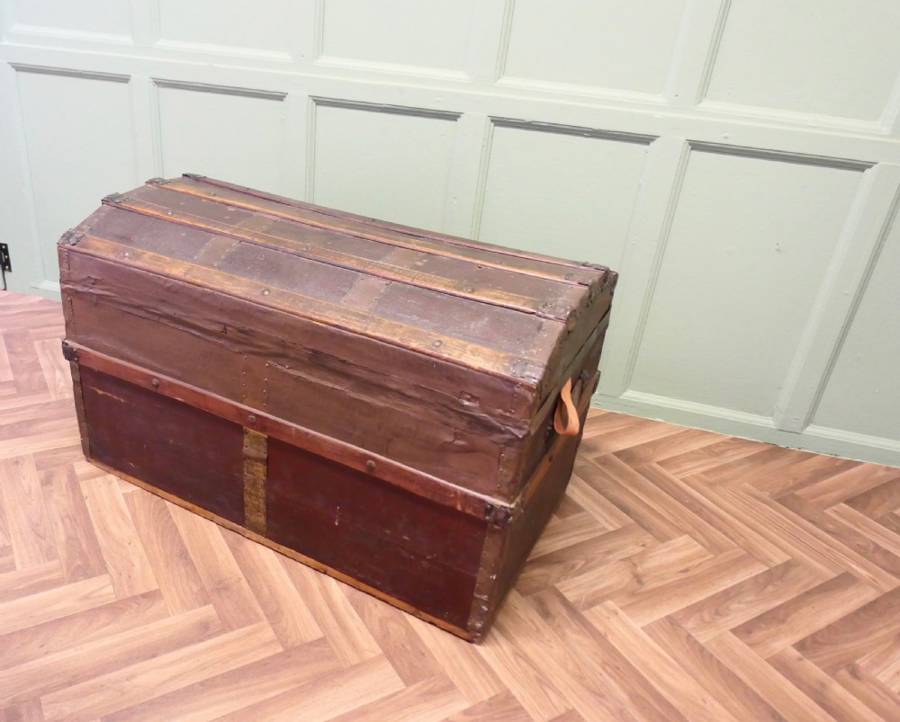 An antique dome top steamer trunk featuring dark canvas casing, polished oak slats, metal banding, and side leather handles. View V