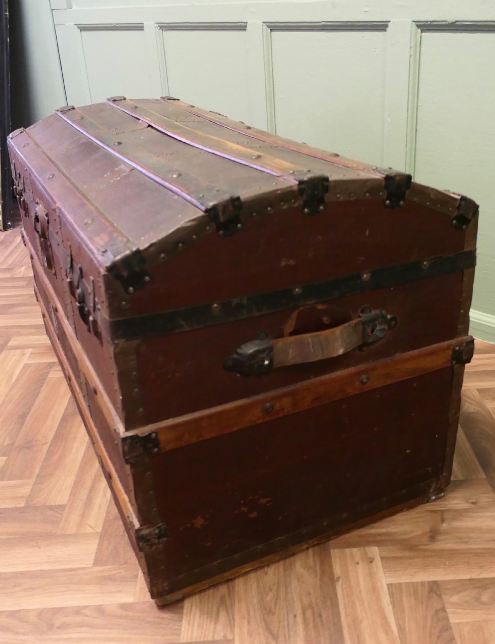 An antique dome top steamer trunk featuring dark canvas casing, polished oak slats, metal banding, and side leather handles. View VI