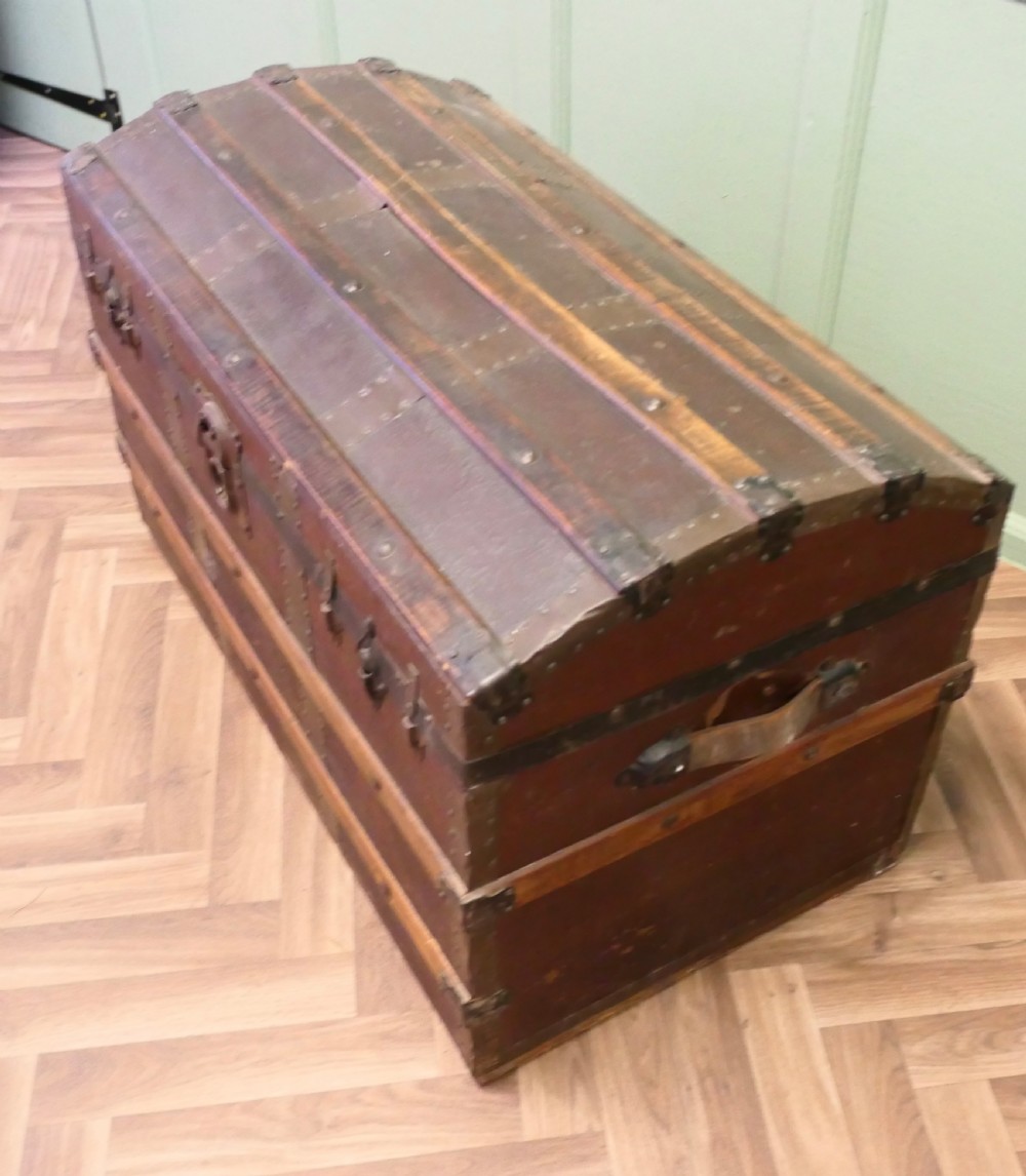 An antique dome top steamer trunk featuring dark canvas casing, polished oak slats, metal banding, and side leather handles. View VII