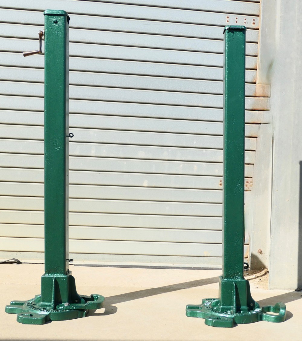 A pair of dark green painted Edwardian metal tennis court net posts featuring mechanical winder handles and heavy cast bases.