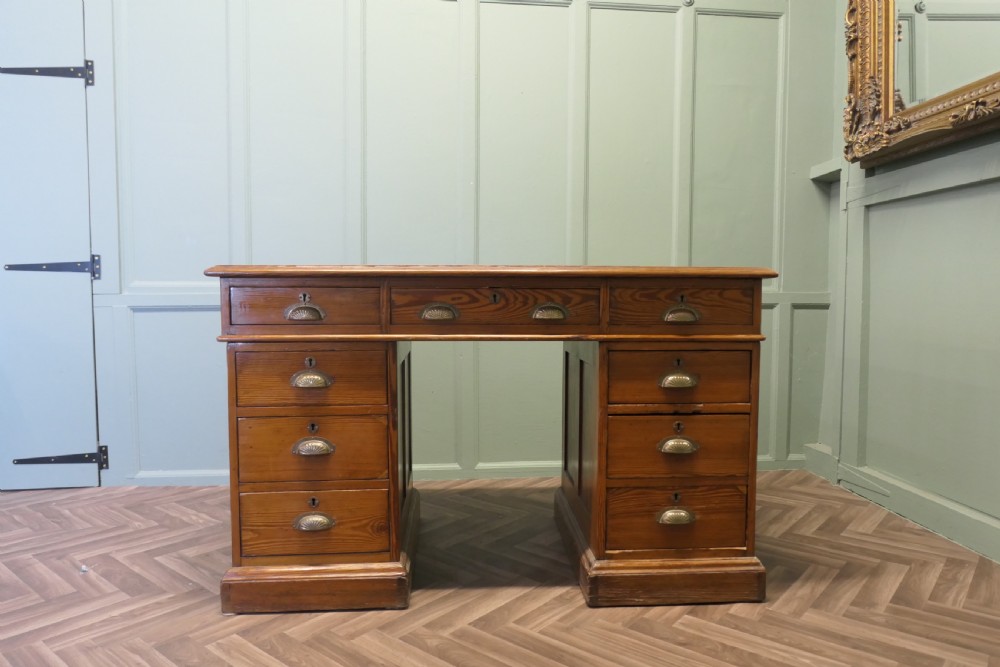 A late Victorian pitch pine pedestal desk featuring nine drawers with brass cup handles and panelled sides.