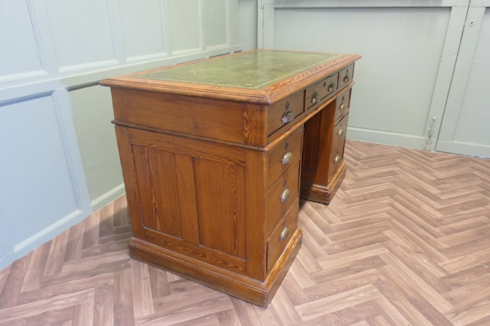 A late Victorian pitch pine pedestal desk featuring nine drawers with brass cup handles and panelled sides. View II