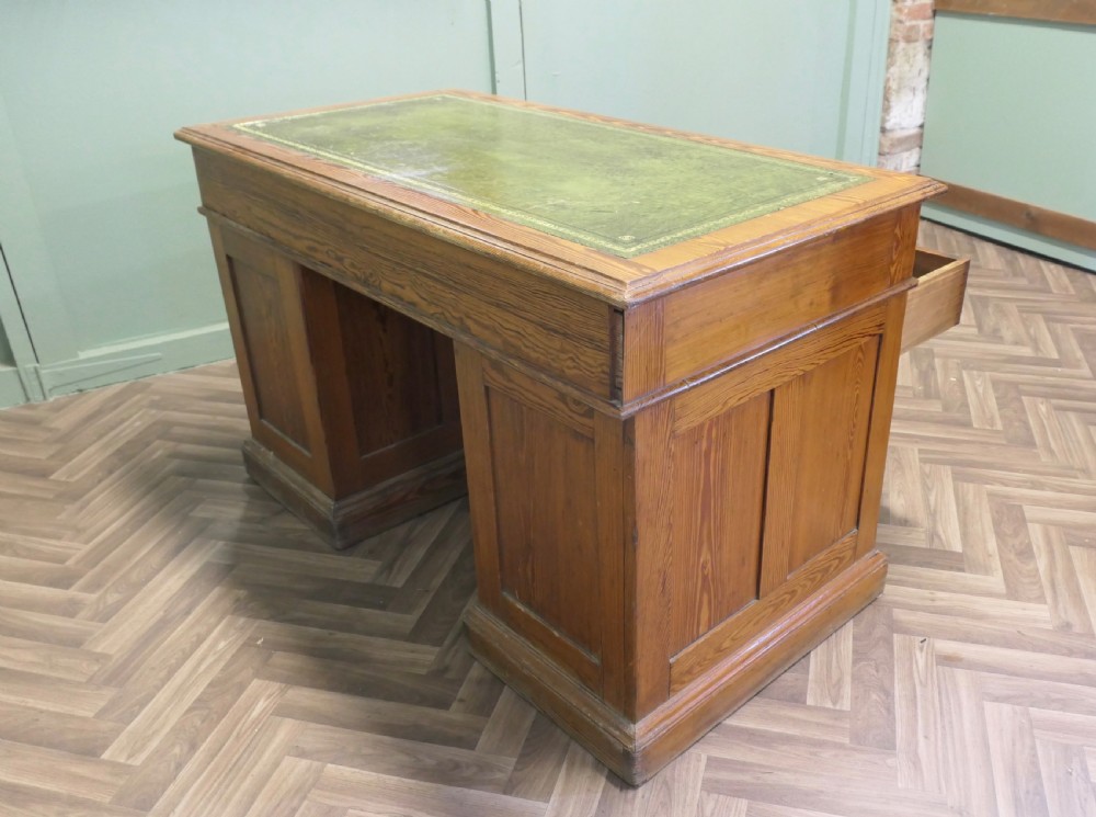 A late Victorian pitch pine pedestal desk featuring nine drawers with brass cup handles and panelled sides. View III