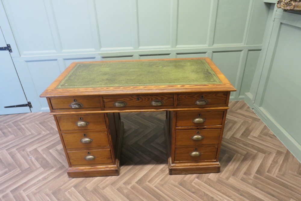A late Victorian pitch pine pedestal desk featuring nine drawers with brass cup handles and panelled sides. View V