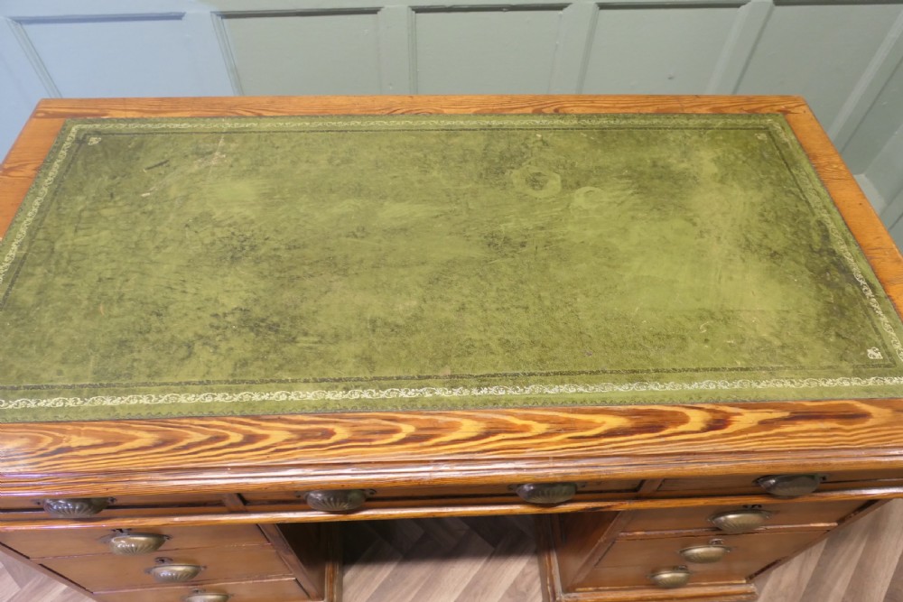 A late Victorian pitch pine pedestal desk featuring nine drawers with brass cup handles and panelled sides. View VI