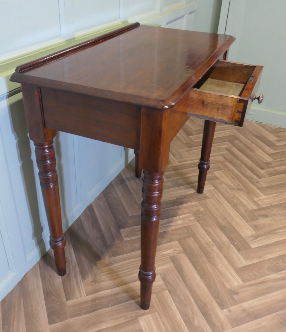 A small Victorian mahogany hall table featuring a rectangular top with a raised rear edge, turned legs, and an open side drawer displaying dovetail joinery.