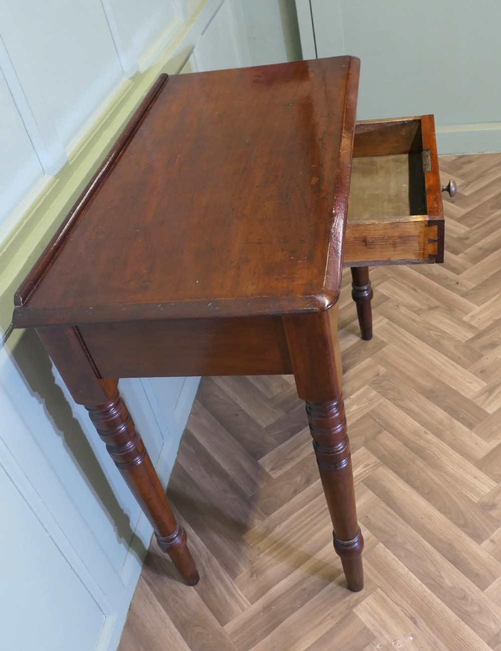 A small Victorian mahogany hall table featuring a rectangular top with a raised rear edge, turned legs, and an open side drawer displaying dovetail joinery. View V
