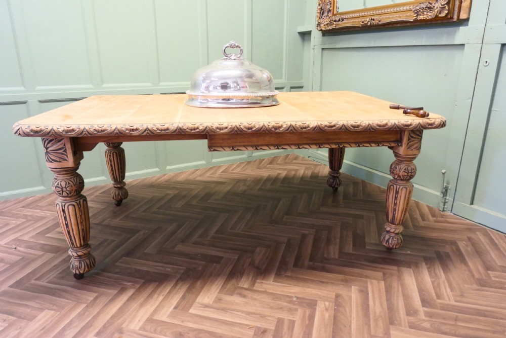 A rectangular bleached oak extending dining table with ornate carved aprons and turned legs. View III