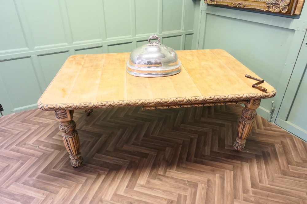 A rectangular bleached oak extending dining table with ornate carved aprons and turned legs. View VII