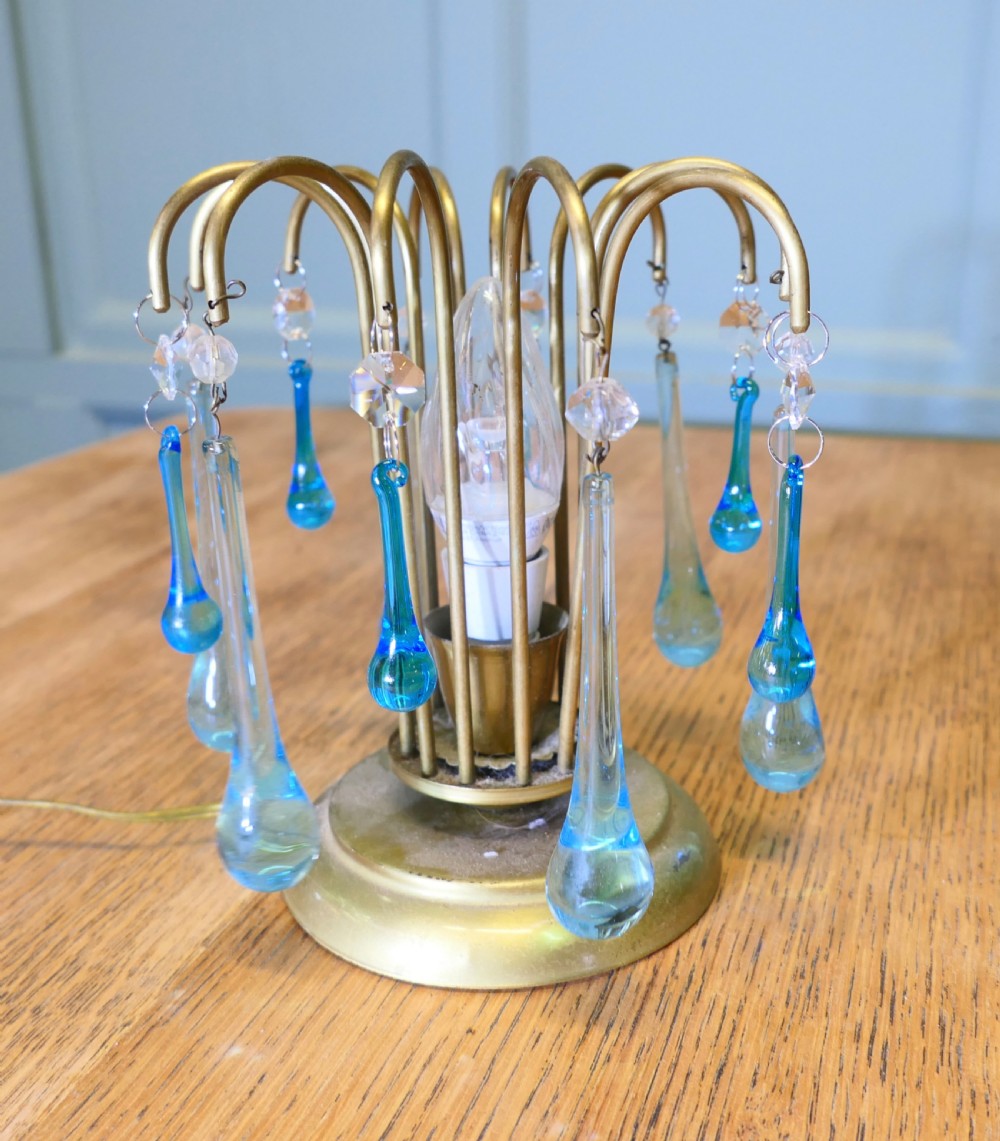 A small brass table lamp featuring curved fountain-like arms adorned with hanging turquoise and clear glass teardrop droplets surrounding a central bulb. View VII
