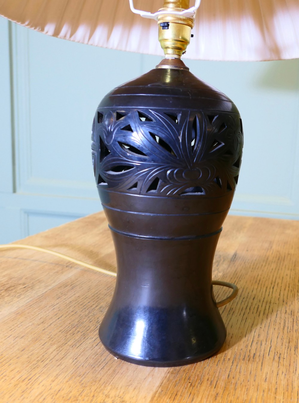 A black ceramic table lamp featuring a carved openwork motif and a cream pleated fabric conical shade. View VI
