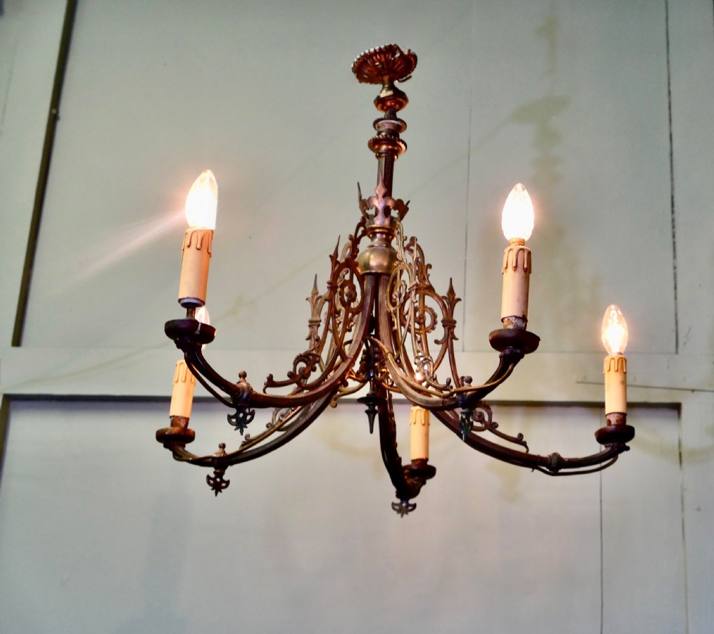 A five-branch gilded brass chandelier featuring Gothic revival openwork tracery, scrolling arms, and candle-style bulb holders.