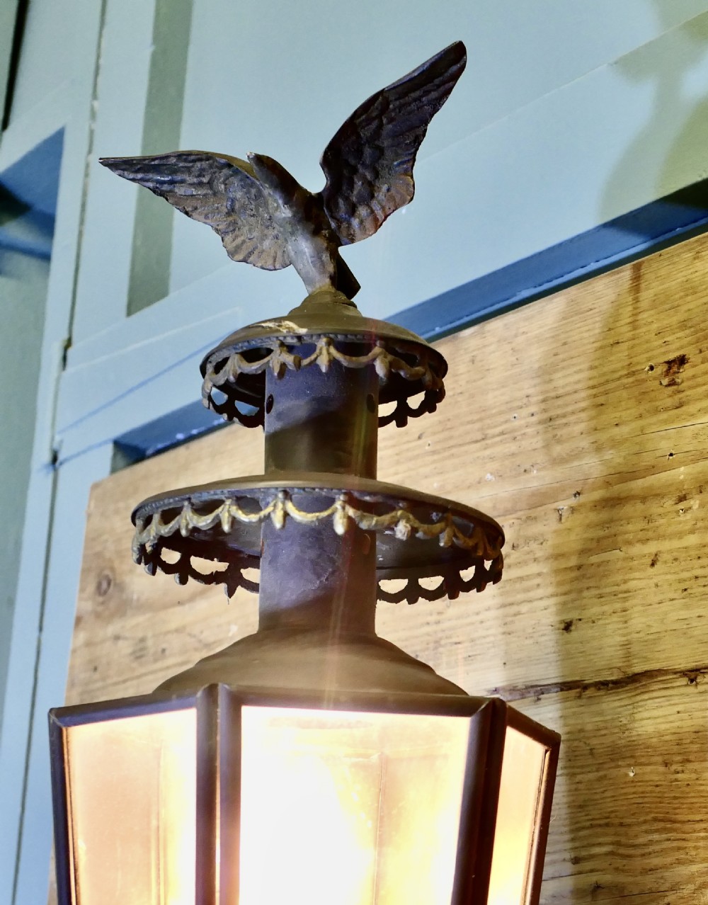 A wall-mounted brass carriage lantern featuring a glazed hexagonal body, decorative pierced collars, a cast eagle finial, and a black wrought scroll bracket. View II