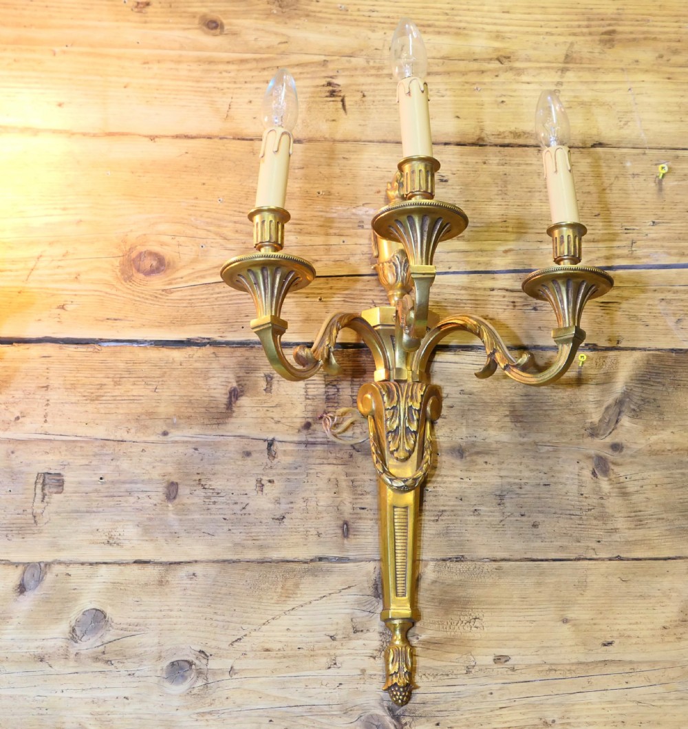 A pair of French Neoclassical cast brass three-light wall sconces featuring acanthus leaf details and urn finials. View II