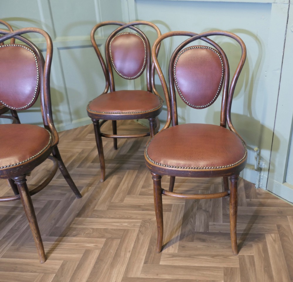 A set of four bentwood bistro dining chairs featuring steam-bent wooden frames and brown leather upholstery detailed with brass studding. View II