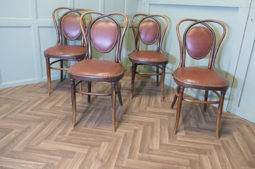 A set of four bentwood bistro dining chairs featuring steam-bent wooden frames and brown leather upholstery detailed with brass studding. View IV