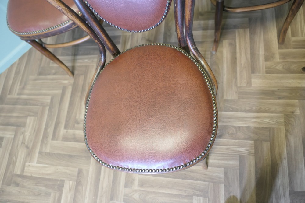 A set of four bentwood bistro dining chairs featuring steam-bent wooden frames and brown leather upholstery detailed with brass studding. View V