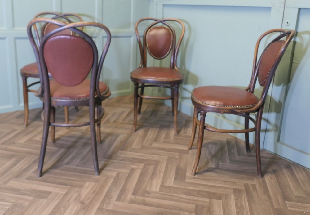 A set of four bentwood bistro dining chairs featuring steam-bent wooden frames and brown leather upholstery detailed with brass studding. View VI
