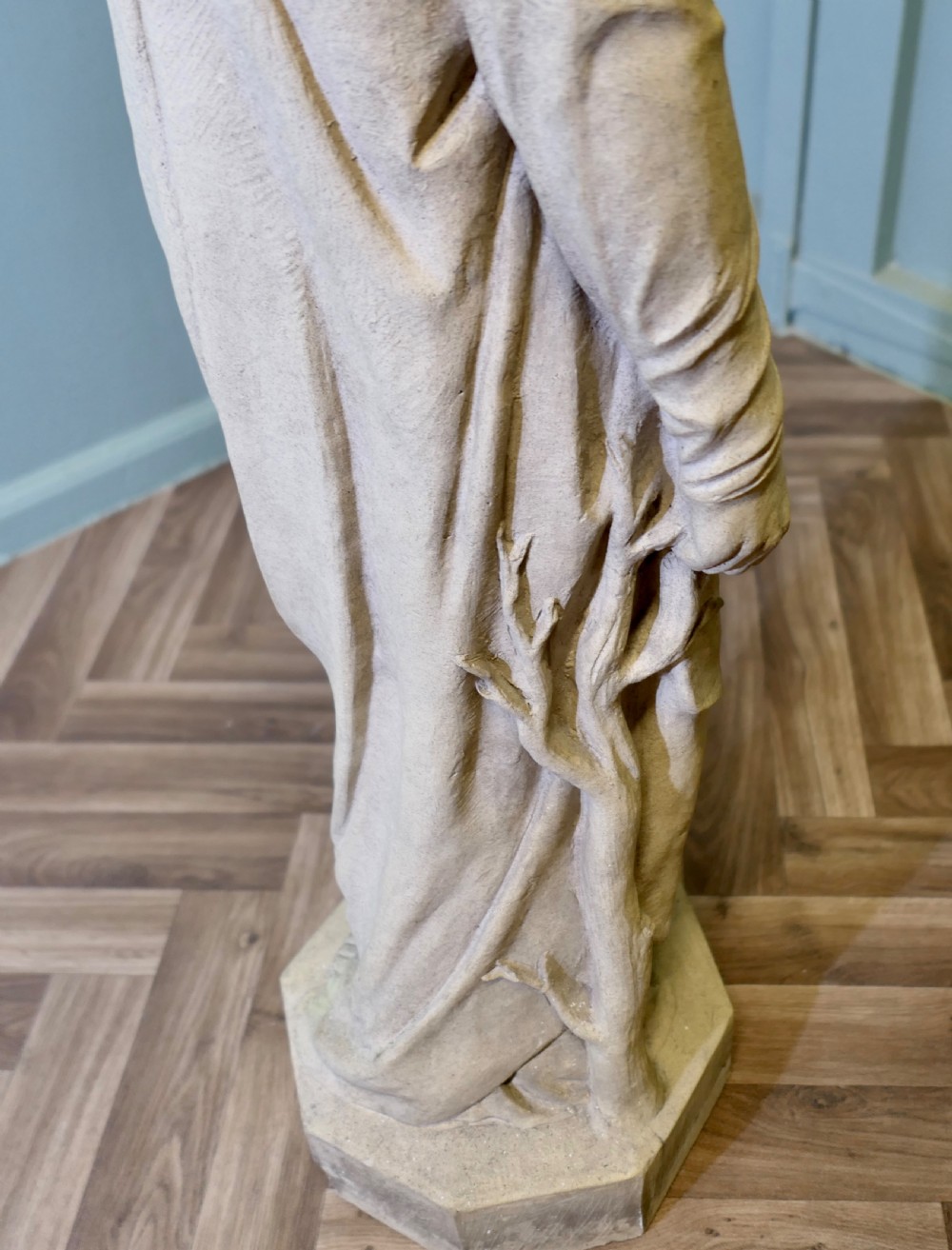 A buff terracotta sculpture of a standing draped female figure wearing a hood, set on an octagonal plinth base. View III