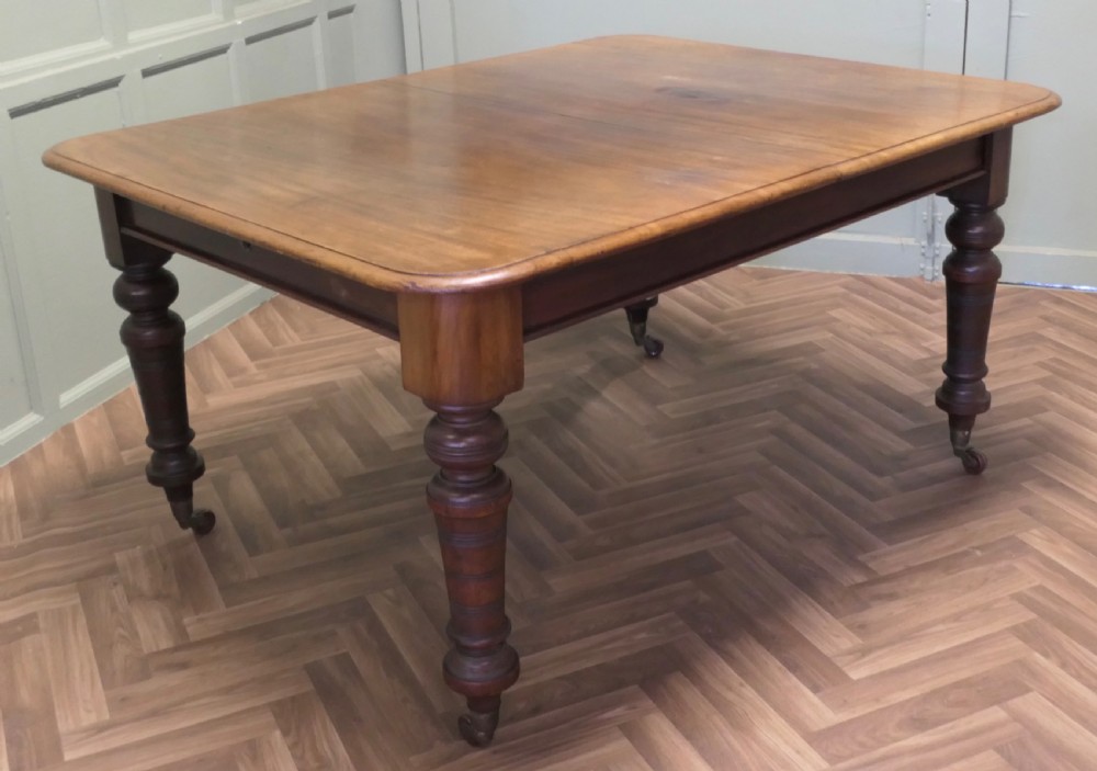 A Victorian extending dining table crafted from warm brown wood with rounded corners, turned legs, and brass castors.