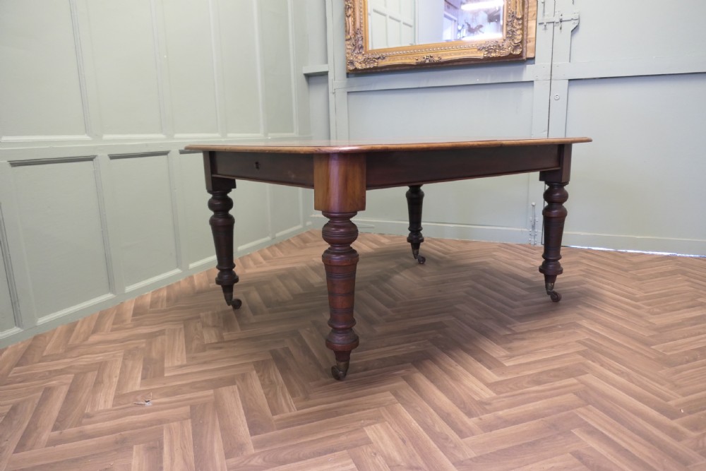 A Victorian extending dining table crafted from warm brown wood with rounded corners, turned legs, and brass castors. View II