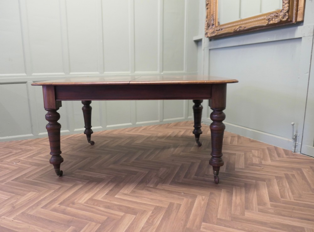 A Victorian extending dining table crafted from warm brown wood with rounded corners, turned legs, and brass castors. View III