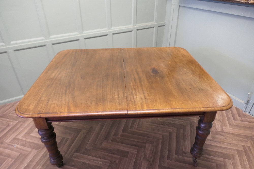 A Victorian extending dining table crafted from warm brown wood with rounded corners, turned legs, and brass castors. View V