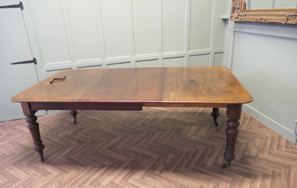A Victorian extending dining table crafted from warm brown wood with rounded corners, turned legs, and brass castors. View VI