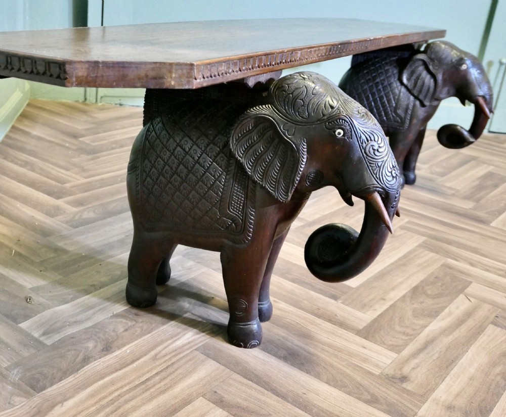 A dark carved wood hall bench featuring a flat rectangular top supported by two detailed elephant figures with raised trunks.