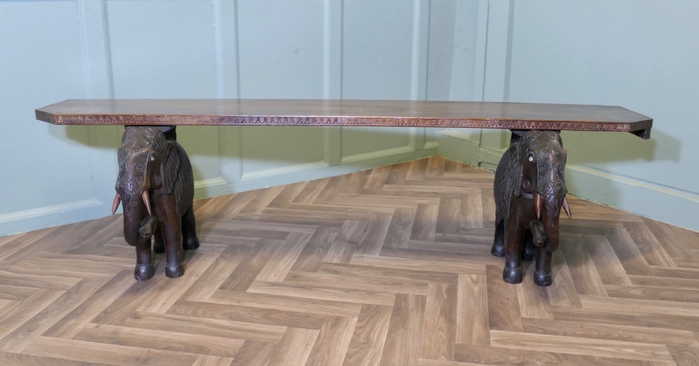 A dark carved wood hall bench featuring a flat rectangular top supported by two detailed elephant figures with raised trunks. View II