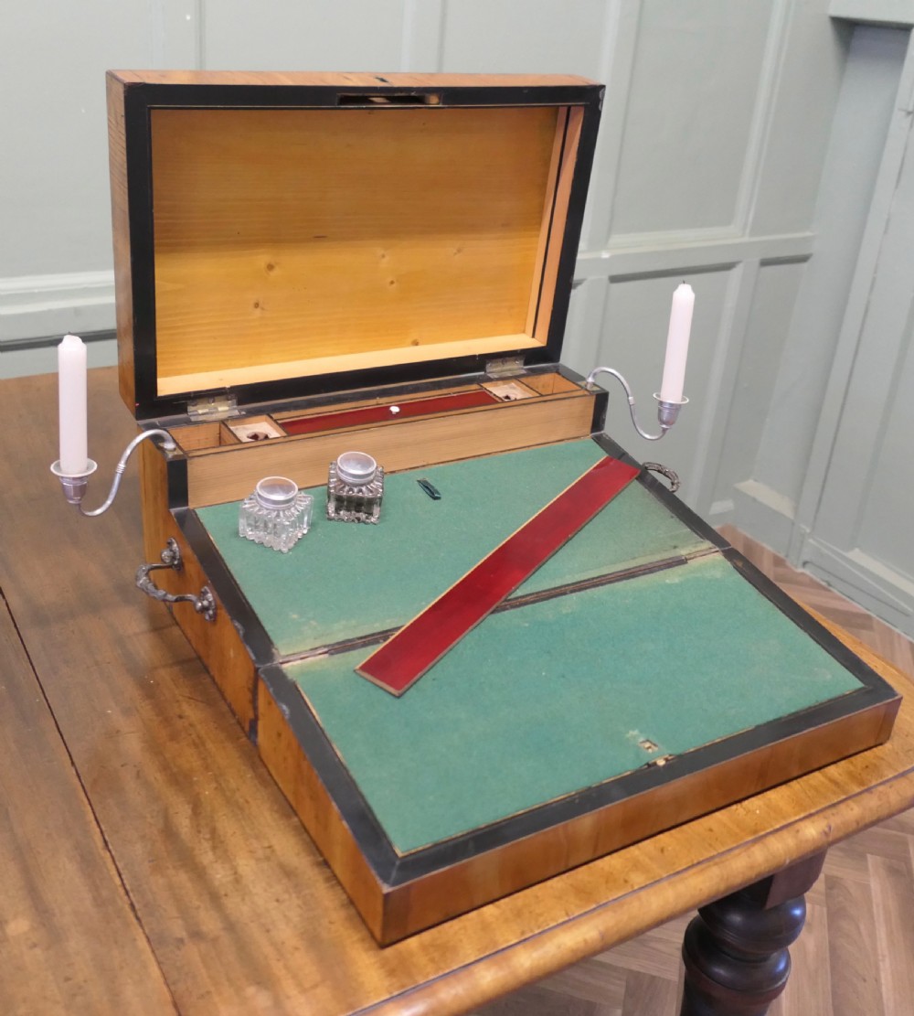 An opened 18th-century satinwood writing slope displaying a green baize writing surface, internal pen tray, glass inkwells, and attached candle sconces.