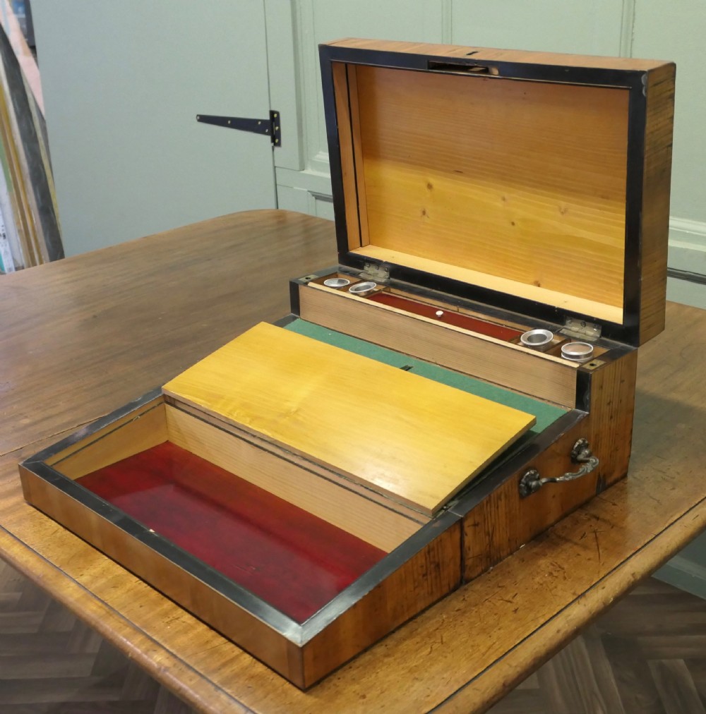 An opened 18th-century satinwood writing slope displaying a green baize writing surface, internal pen tray, glass inkwells, and attached candle sconces. View V