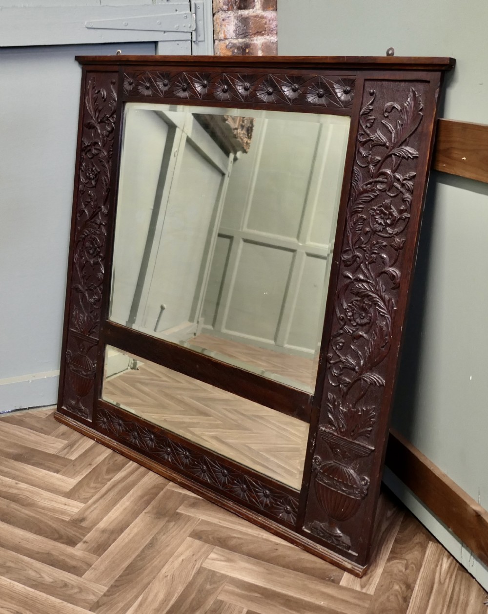 A large rectangular dark oak wall mirror featuring hand-carved foliate side panels, carved urn motifs, a rosette border, and two glass panes.