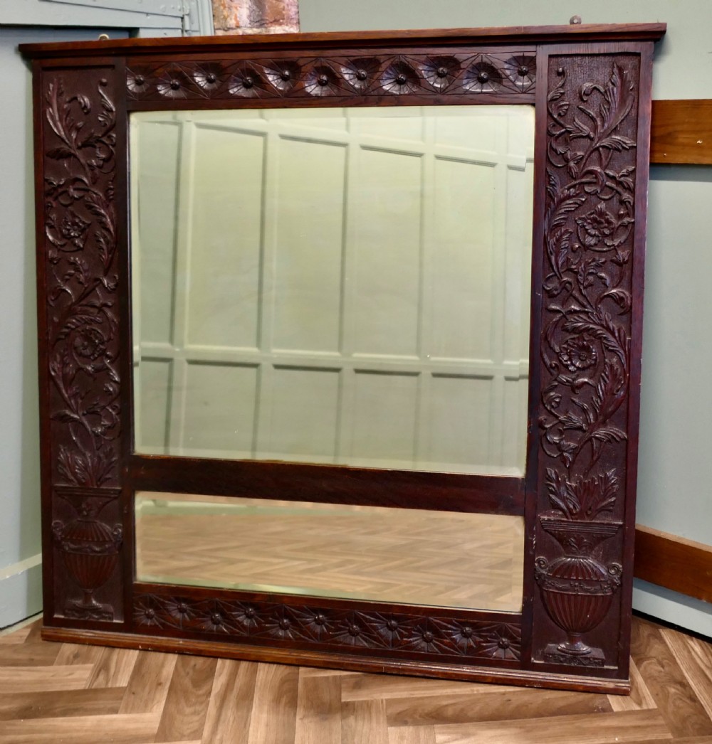 A large rectangular dark oak wall mirror featuring hand-carved foliate side panels, carved urn motifs, a rosette border, and two glass panes. View II