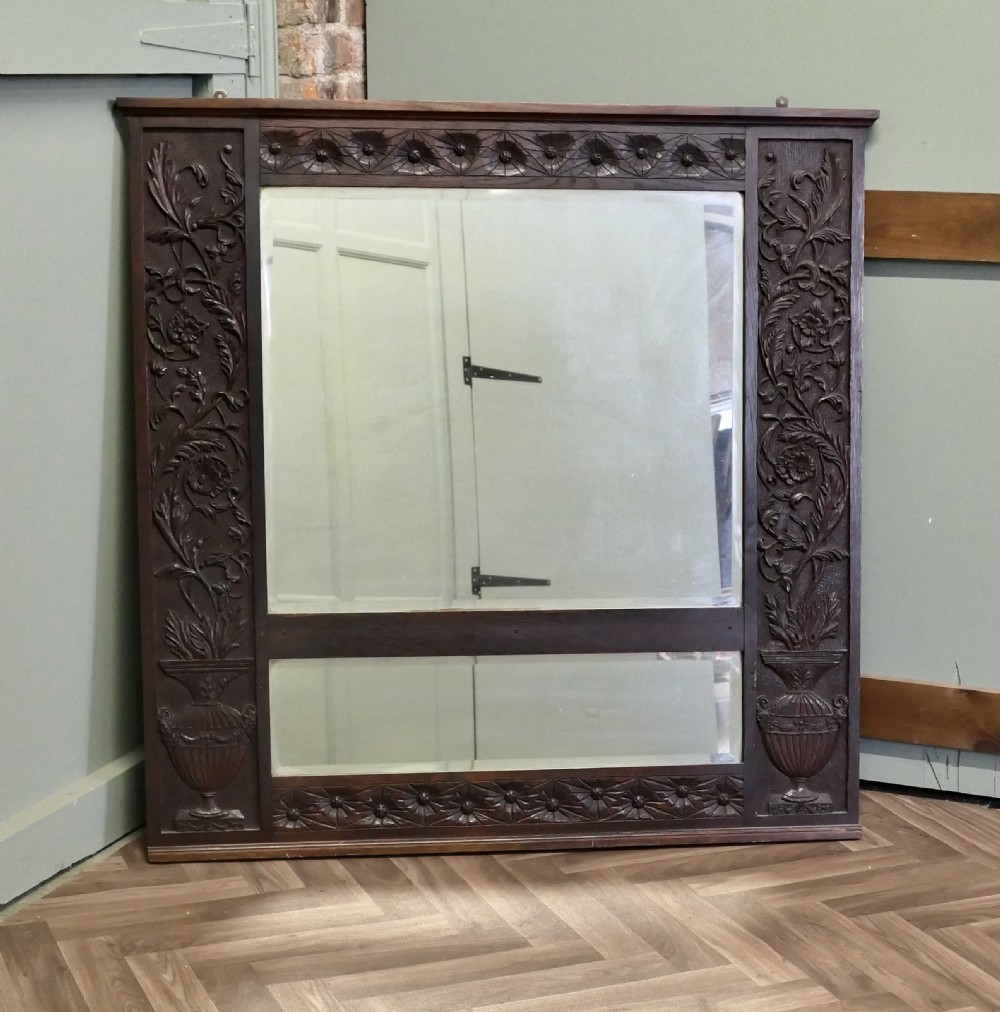 A large rectangular dark oak wall mirror featuring hand-carved foliate side panels, carved urn motifs, a rosette border, and two glass panes. View IV