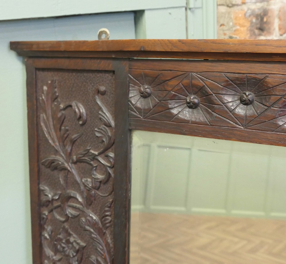 A large rectangular dark oak wall mirror featuring hand-carved foliate side panels, carved urn motifs, a rosette border, and two glass panes. View V