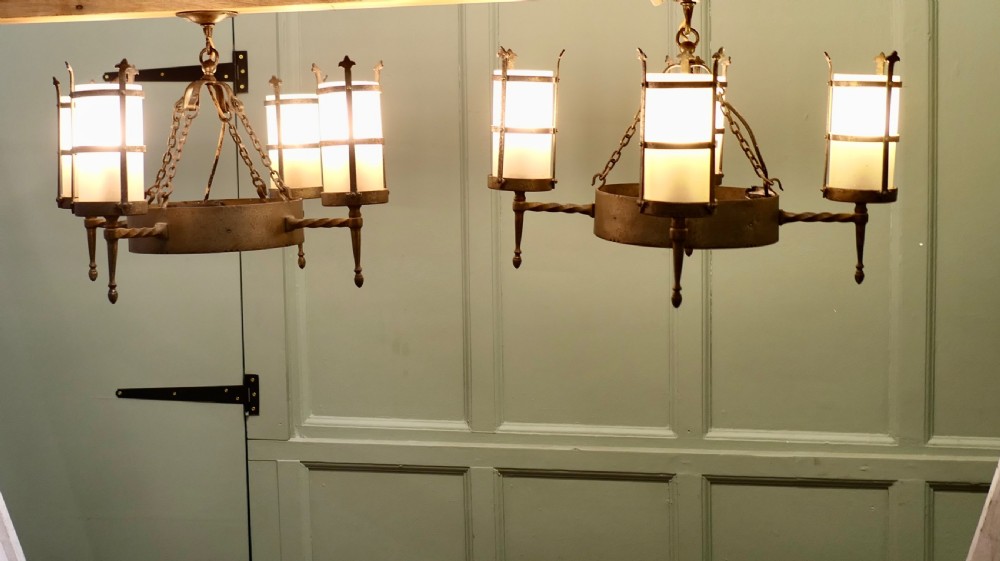 A pair of Arts and Crafts four-arm ceiling lights featuring twisted metal arms, cylindrical frosted shades, and chain suspensions.