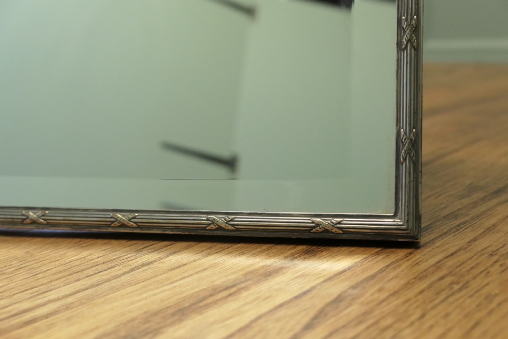 An arched French Art Deco silver-plated vanity mirror featuring bevelled glass and a decorative ribbon cresting. View II